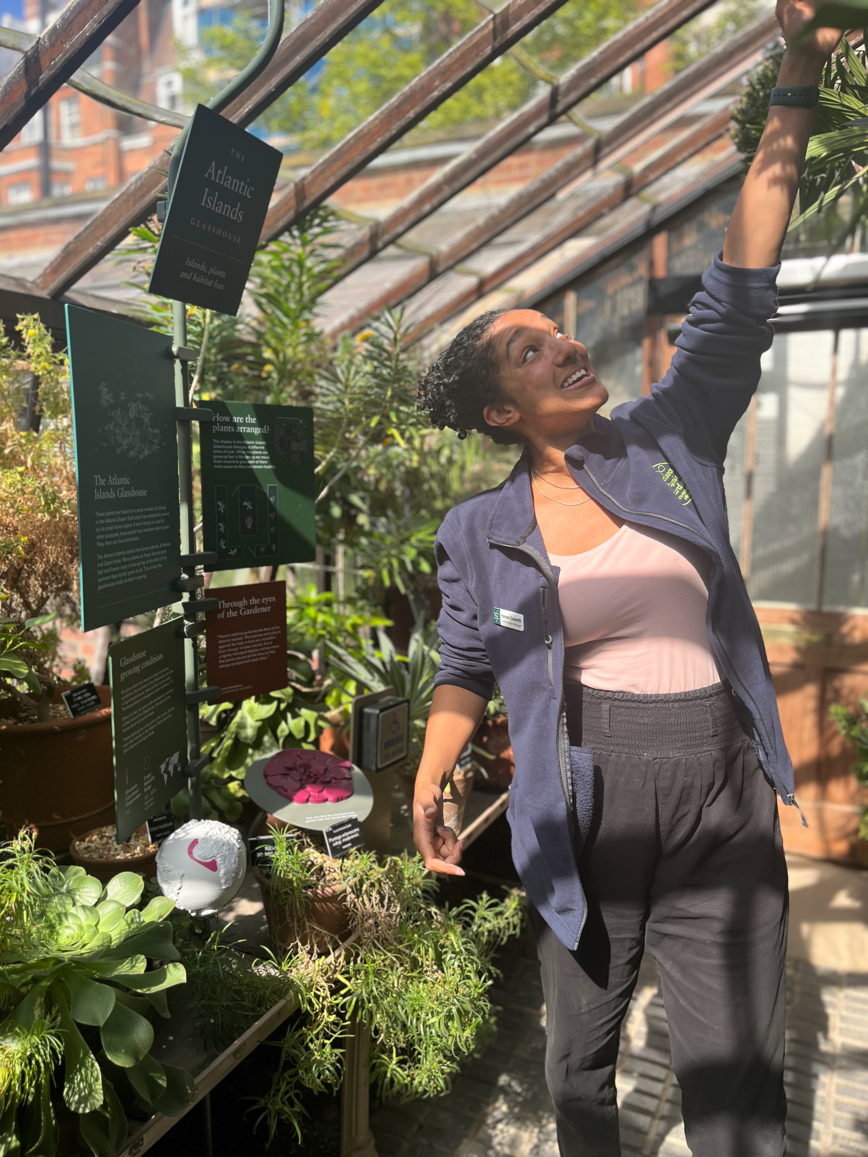 Hannah standing in a glasshouse talking animatedly about plants