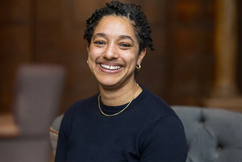 Hannah Cusworth, a headshot of Black woman smiling wearing a navy blue jumper and gold chain